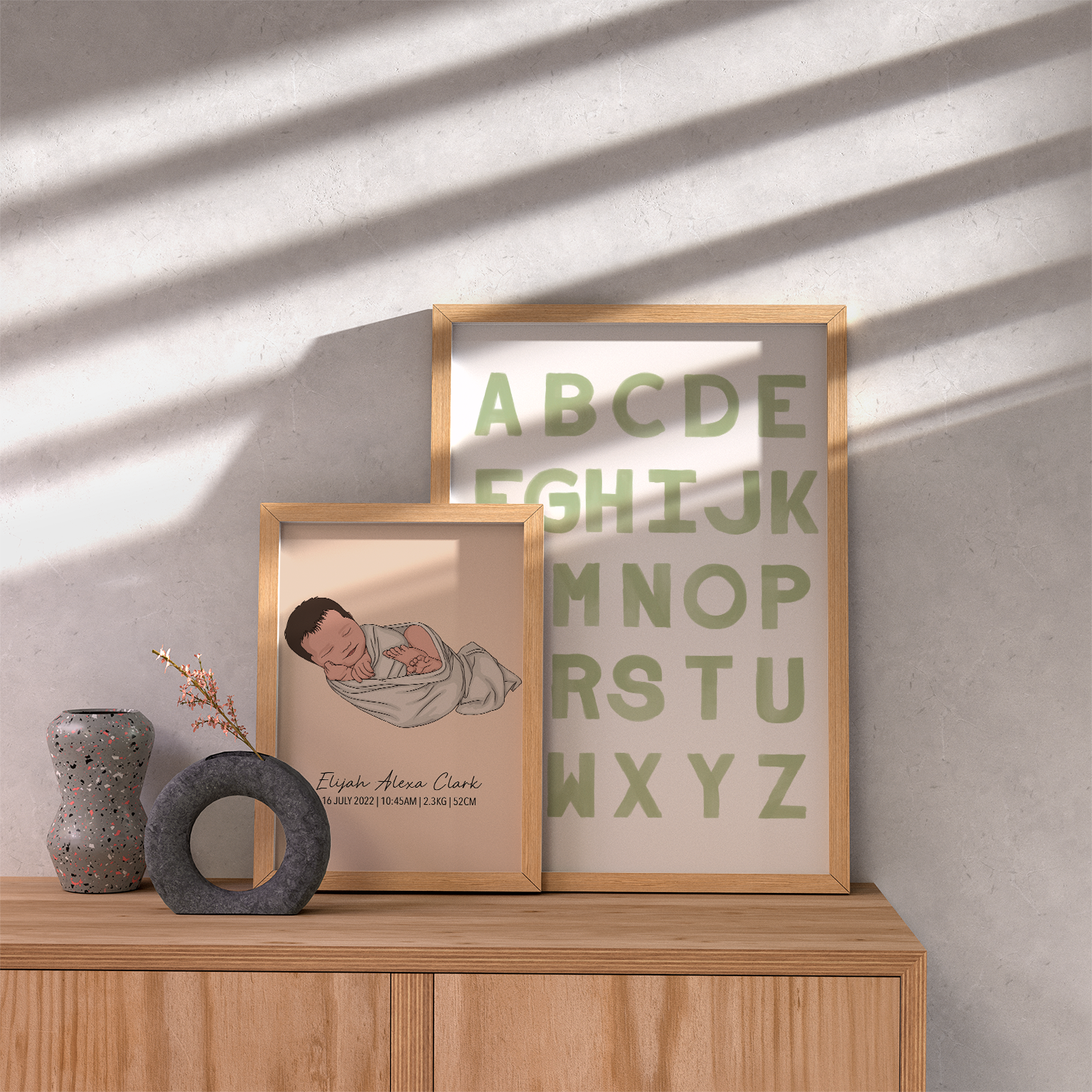 A set of two framed watercolour prints with letters and numbers, and a personalized text element, displayed on a wooden shelf with a decorative vase and a round object to the left.